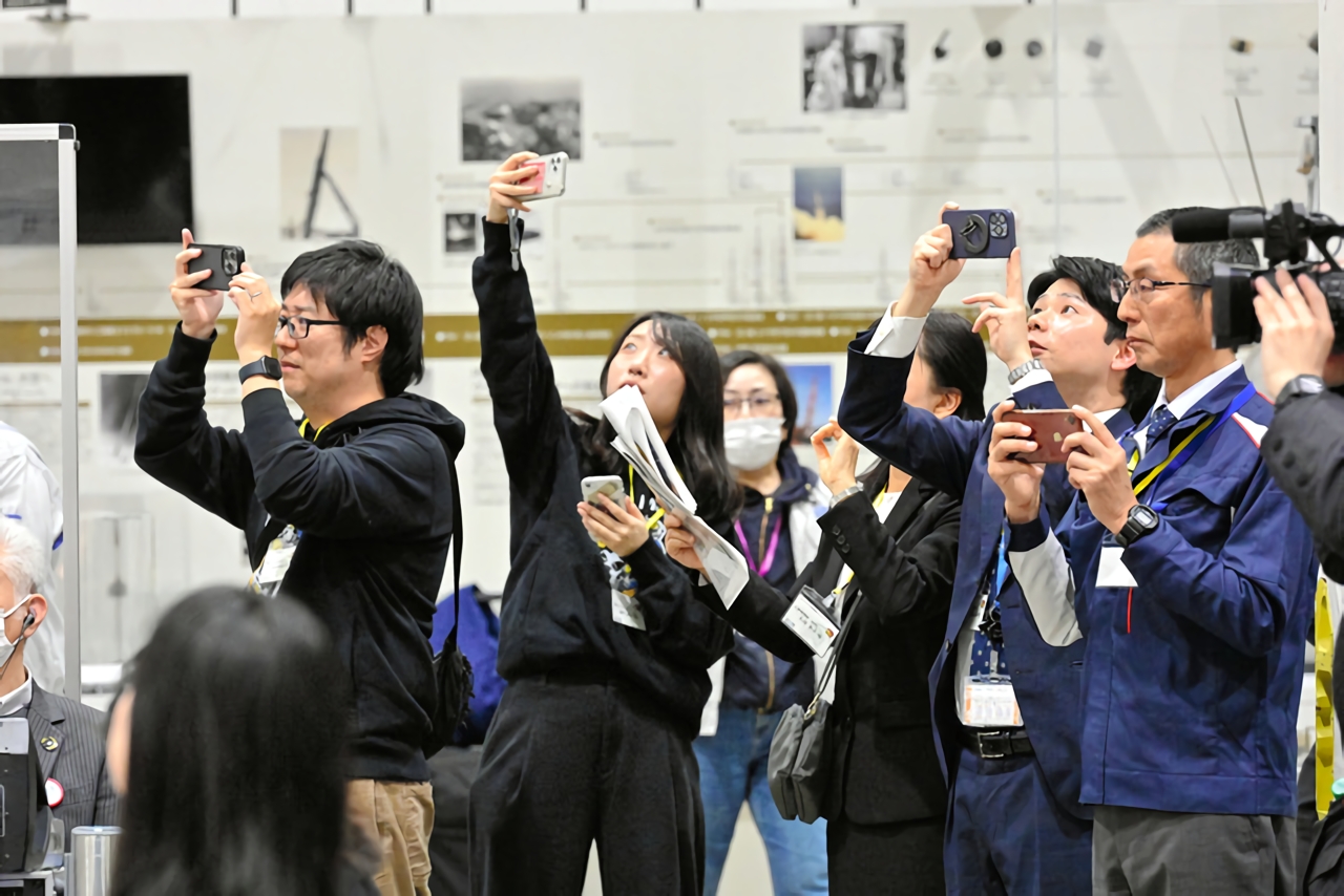 無人探査機SLIMの着陸間際に、記者会見場でライブ配信されていた動画画面にスマートフォンを向けるプロジェクトの関係者ら=2024年1月20日午前0時20分、神奈川県相模原市、角野貴之撮影