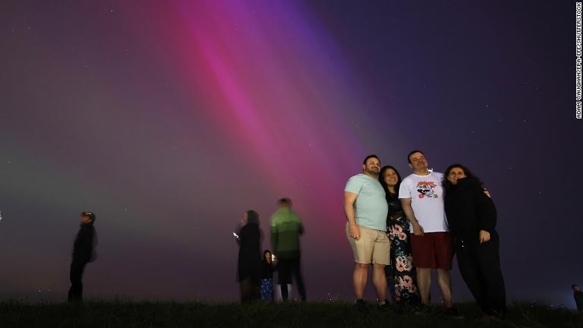 北のオーロラを背景に写真撮影のポーズを取る人々＝１０日、英イングランド・クロスビー/Adam Vaughan/EPA-EFE/Shutterstock